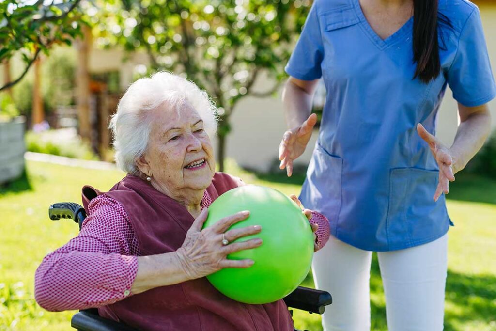 Older adult sitting at a dining table while a staff member prepares daily medications in a pill organizer.